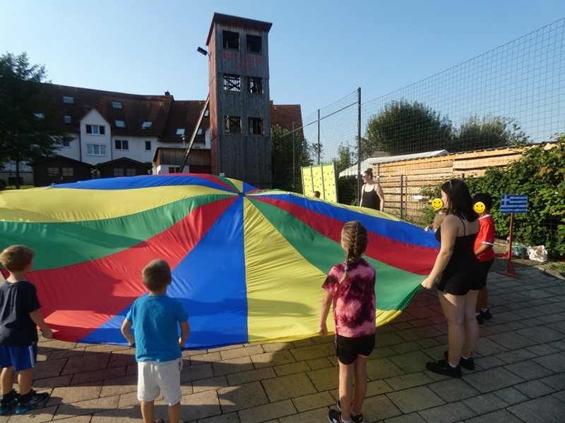 Kinder und Auszubildende halten und spielen mit einem großen, bunten Schwingtuch.