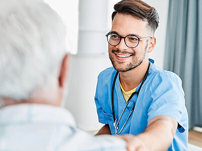 Auf dem Bild sieht man eine Pflegekraft, der mit einem Patienten spricht.